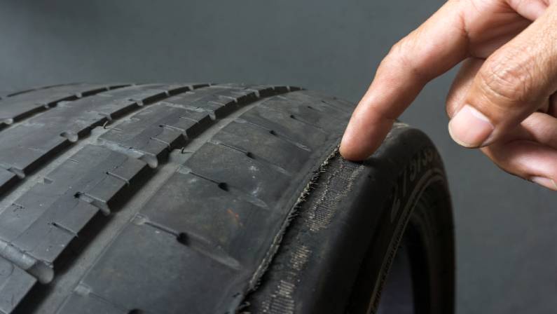 Finger pointing to damage on tire tread.