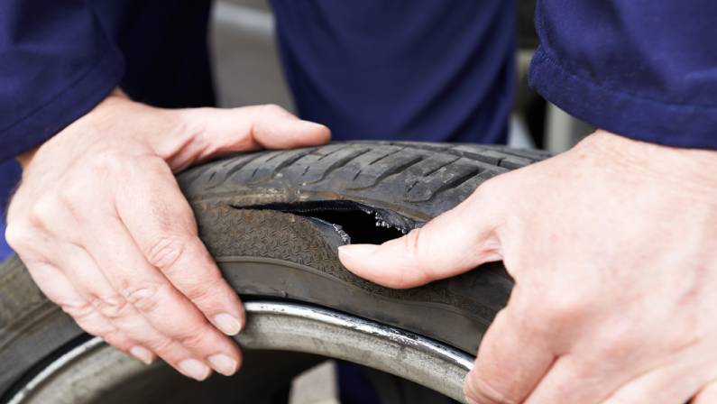 Close Up Of Mechanic Examining Damaged Car Tyre