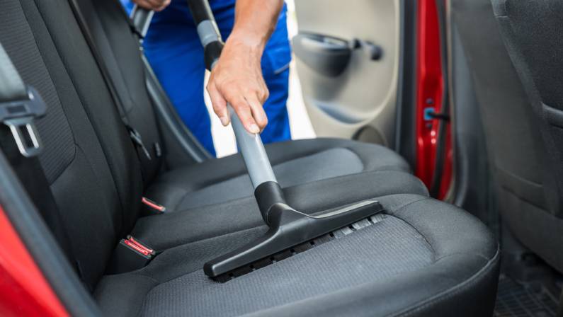 Handyman vacuuming car back seat with vacuum cleaner