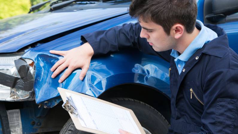Auto Workshop Mechanic Inspecting Damage To Car And Filling In Repair Estimate
