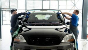 Automobile special workers replacing windscreen or windshield of a car in auto service station garage.