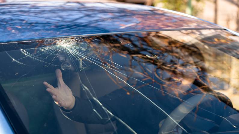 Shocked woman in car with broken windshield and cracks.