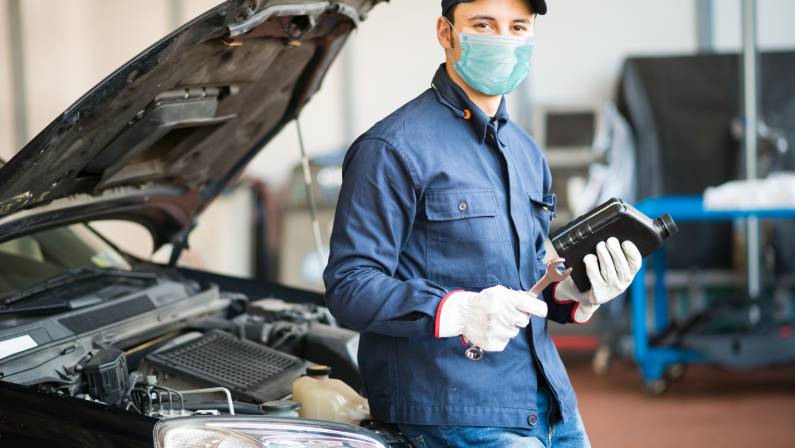 Masked car mechanic holding a jug of motor oil