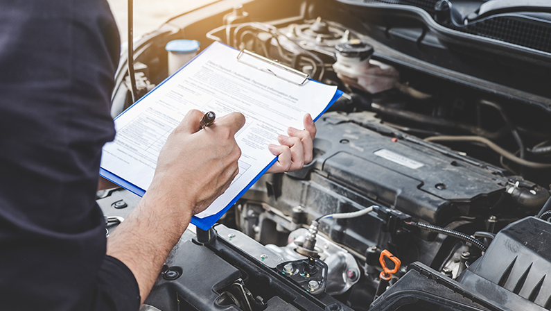 Automobile mechanic repairman checking a car engine with inspecting writing to the clipboard the checklist for car service and maintenance.