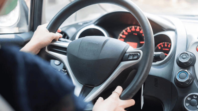 Young woman wearing protective face mask and hand controlling steering wheel in her car.