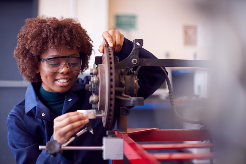 Female Student Working On Car Brakes On Auto Mechanic Apprenticeship Course At College