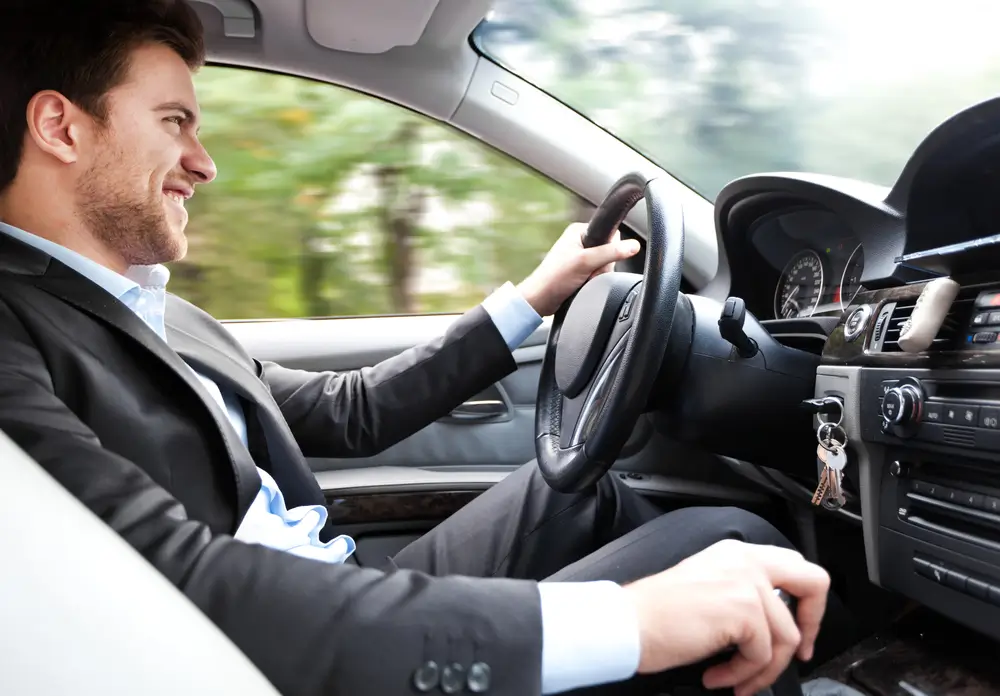 Smiling businessman driving and shifting gears, demonstrating the smooth operation of the transmission in a car.