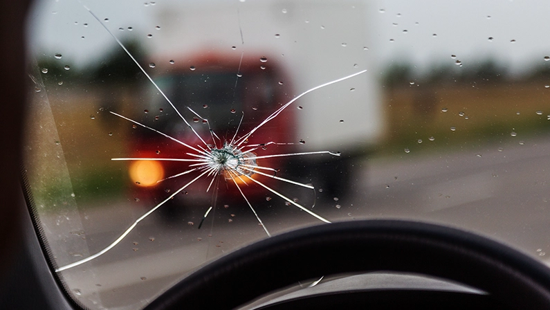 Broken windshield of a car. A web of radial splits, cracks on the triplex windshield. Broken car windshield, damaged glass with traces of oncoming stone on road or from bullet trace in car glass