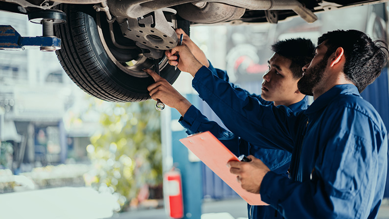 Car repair service. Two professional look technicians inspecting car underbody and suspension system by using check list in modern car service shop. Professional occupation teamwork.