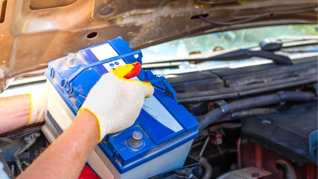 A male car mechanic takes out a battery from under the hood of a auto to repair, charge or replace it.