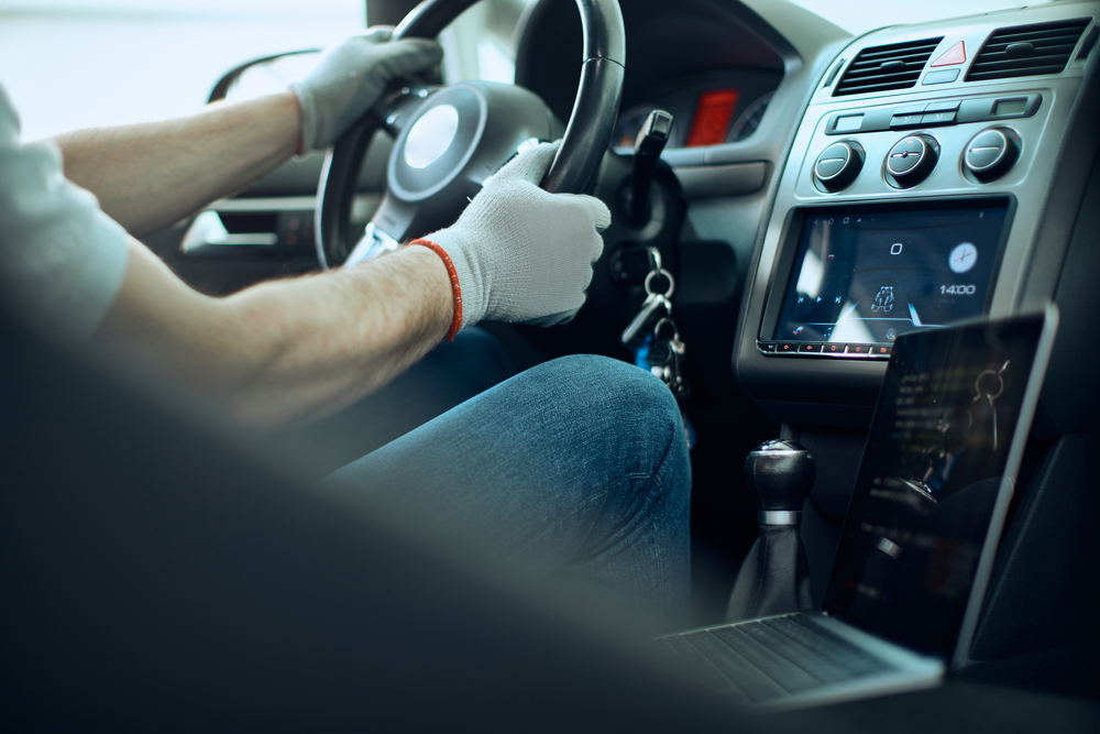 Close-up of auto repairman sitting behind steering wheel while running car diagnostic on laptop in a workshop.