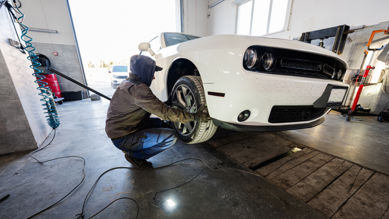 Mechanic in service repair station working with muscle car. Man worker jacks up the car to diagnose the chassis.