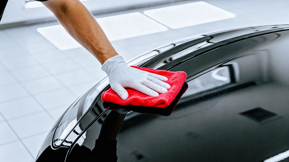 A gloved hand carefully cleans a black car's surface, ensuring a flawless, reflective shine.