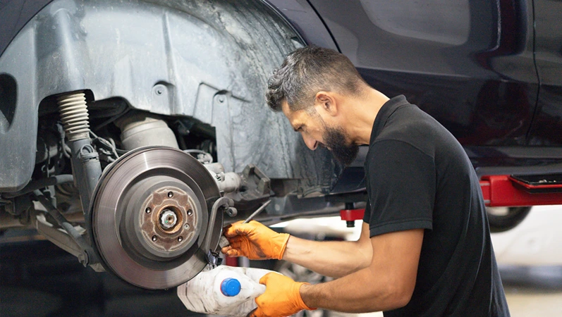 Auto mechanic performing routine brake fluid change on a lifted car
