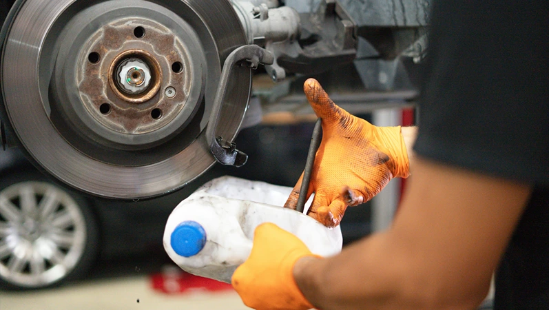 Mechanic wearing orange gloves inspecting a car's brake disc and caliper in an auto workshop